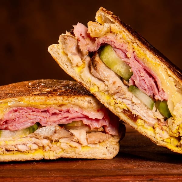 A Cuban sandwich, cut in half, revealing layers of ham, pork, cheese, pickles, and mustard.